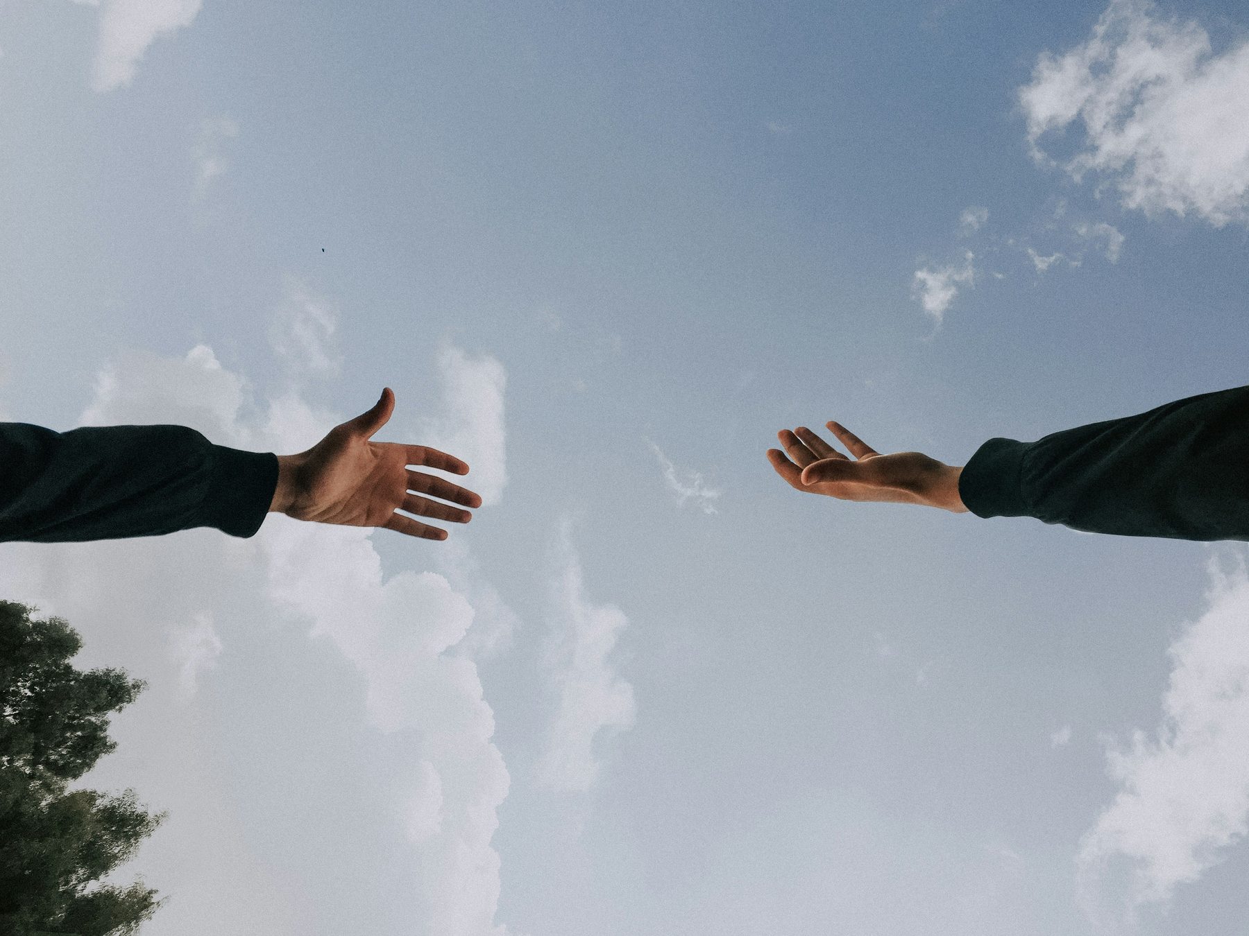 Two people reaching toward one another beneath an open sky.